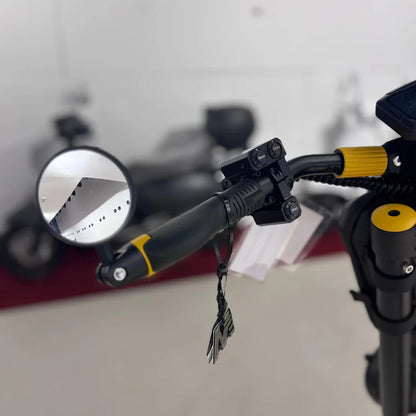 Izdelek je električni skiro znamke Vsett, model Vsett 11 Super. Na sliki je prikazan del krmila skiroja, ki vključuje ogledalo, gumirane ročaje in kontrolne gumbe za različne načine vožnje. V ozadju so vidni tudi drugi skiroji. Celoten izgled nakazuje na moderno obliko in funkcionalnost.