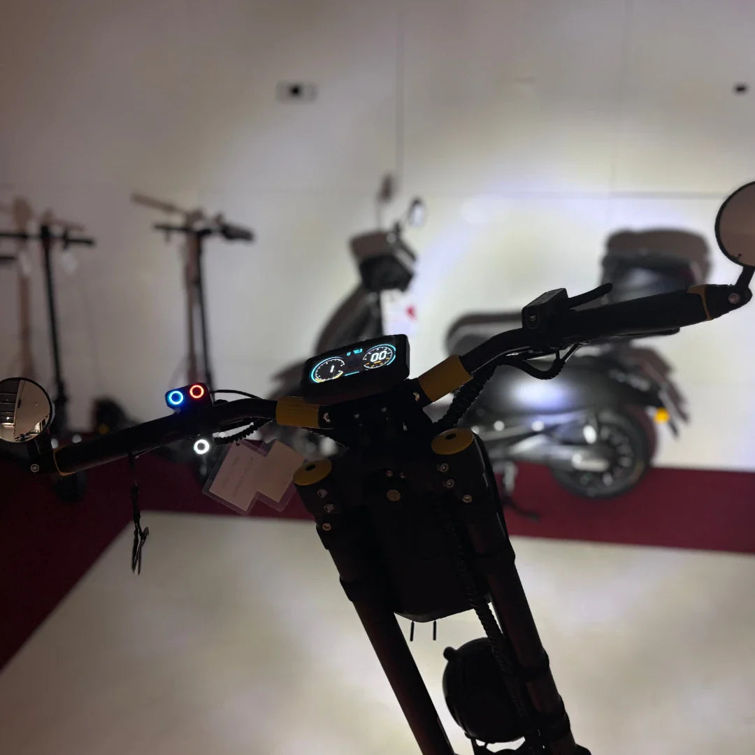 Na sliki je električni skiro znamke Vsett, model 11 Super. Vidni so krmili s prikazovalnikom, ki prikazuje hitrost in druge informacije. Na krmilu so tudi luči in ogledala, kar nakazuje na funkcionalnost in varnost pri vožnji. V ozadju so še drugi skiroji, kar daje občutek razstave ali prodajnega prostora.