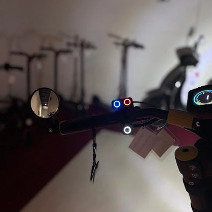 Na sliki je električni skiro znamke Vsett, model 11 Super. Vidna je sprednja stran krmila, kjer so nameščeni luči v rdeči in modri barvi ter ogledalo za boljšo vidljivost. V ozadju so drugi skiroji, kar nakazuje, da gre za prodajni prostor.