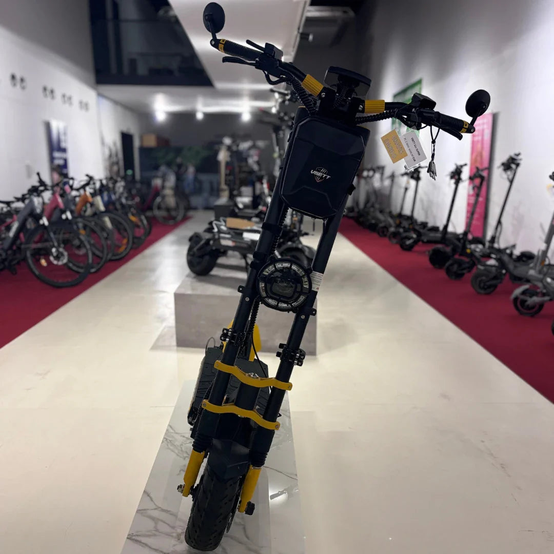 Na sliki je električni skiro znamke Vsett, model 11 Super. Vidimo ga postavljen na prodajnem prostoru, kjer so v ozadju tudi drugi električni skiroji. Izdelek ima robustno konstrukcijo, široke pnevmatike in značilno obliko, kar nakazuje na njegovo zmogljivost in stabilnost. Rdeča preproga v ozadju dodaja kontrast in poudarja izdelek.