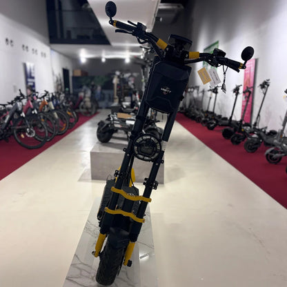 Na sliki je električni skiro znamke Vsett, model 11 Super. Vidimo ga postavljen na prodajnem prostoru, kjer so v ozadju tudi drugi električni skiroji. Izdelek ima robustno konstrukcijo, široke pnevmatike in značilno obliko, kar nakazuje na njegovo zmogljivost in stabilnost. Rdeča preproga v ozadju dodaja kontrast in poudarja izdelek.