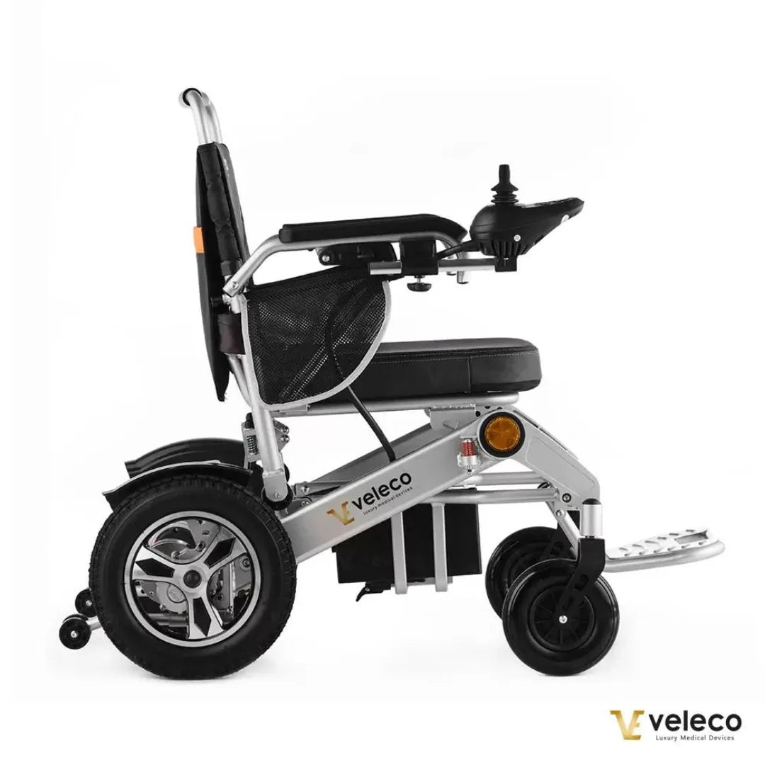 Izdelek na sliki je električni invalidski voziček znamke Veleco, model Cosmo. Voziček ima sodobno zasnovo z robustnim aluminijastim okvirjem in udobnim sedežem. Vidni so veliki kolesi, ki omogočajo enostavno premikanje, ter ročica za upravljanje, ki omogoča enostavno manevriranje.