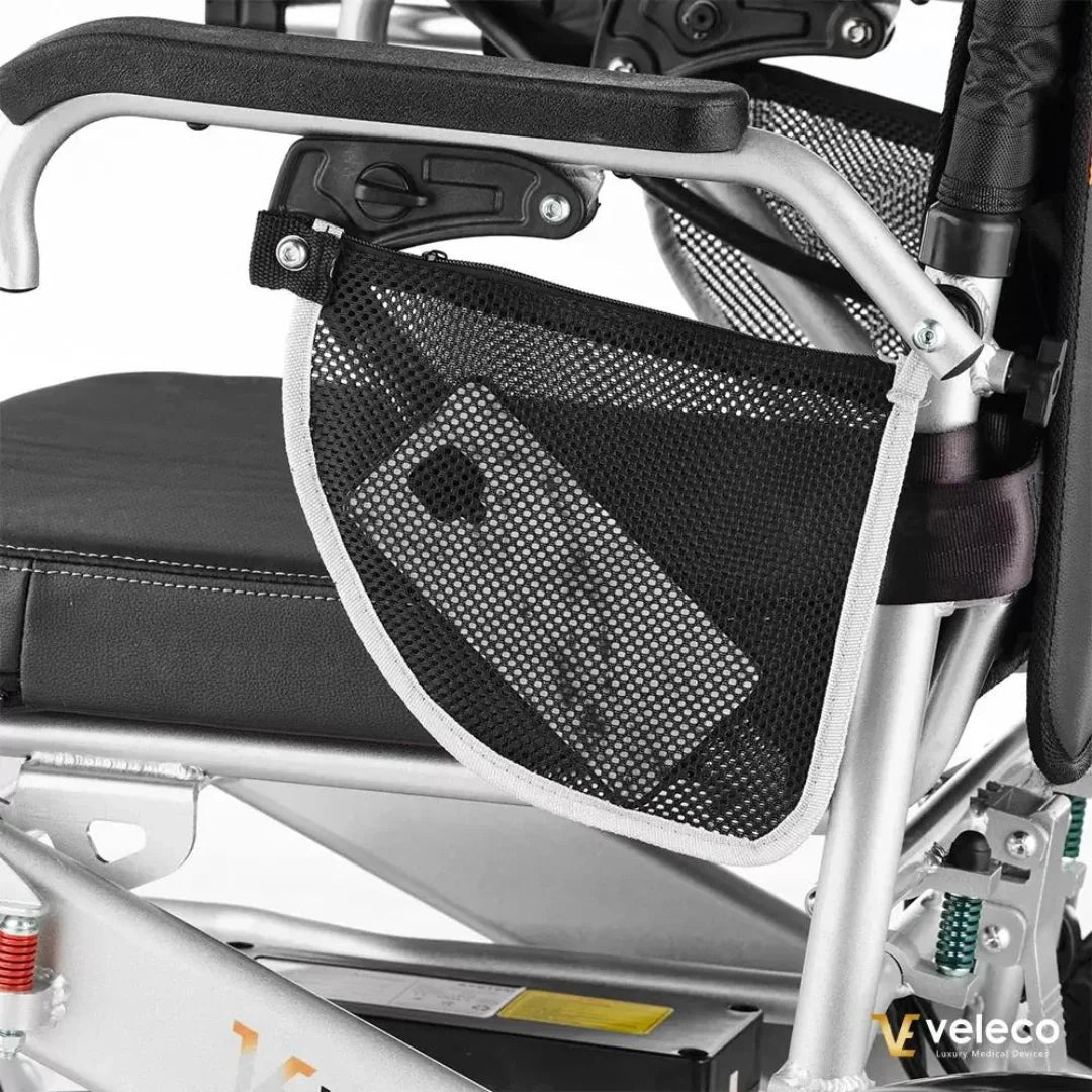 Izdelek na sliki je električni invalidski voziček znamke Veleco, model Cosmo. Na sliki je vidna podrobnost naslonjala, kjer je pritrjena mrežasta torbica, v kateri je shranjen mobilni telefon. Voziček ima robustno aluminijasto konstrukcijo in udobno oblazinjenje.