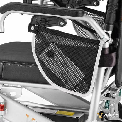 Izdelek na sliki je električni invalidski voziček znamke Veleco, model Cosmo. Na sliki je vidna podrobnost naslonjala, kjer je pritrjena mrežasta torbica, v kateri je shranjen mobilni telefon. Voziček ima robustno aluminijasto konstrukcijo in udobno oblazinjenje.