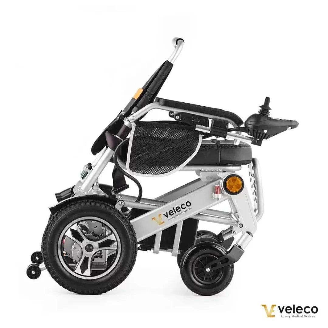 Izdelek na sliki je električni invalidski voziček, model Veleco Cosmo. Na sliki je prikazan voziček v stranski perspektivi, ki ima moderno zasnovo z aluminijastim okvirjem in udobnim sedežem. Vidne so tudi kolesa, ena večja in dve manjših, ter upravljalna ročka, ki omogoča enostavno manevriranje. Voziček je zasnovan za udobno in praktično uporabo.