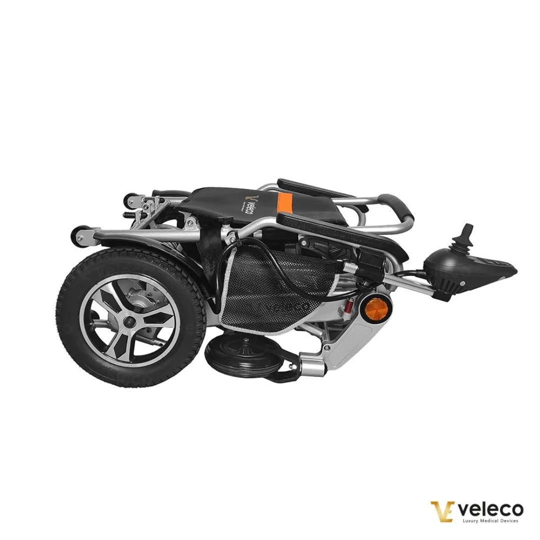 Izdelek na sliki je električni invalidski voziček, model Veleco Cosmo. Na sliki je prikazan zložen voziček, ki ima kompaktno zasnovo in je opremljen s kolesi ter upravljalnikom. Zasnova je moderna in funkcionalna, kar omogoča enostavno prenašanje in shranjevanje.
