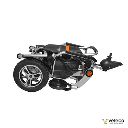 Izdelek na sliki je električni invalidski voziček, model Veleco Cosmo. Na sliki je prikazan zložen voziček, ki ima kompaktno zasnovo in je opremljen s kolesi ter upravljalnikom. Zasnova je moderna in funkcionalna, kar omogoča enostavno prenašanje in shranjevanje.