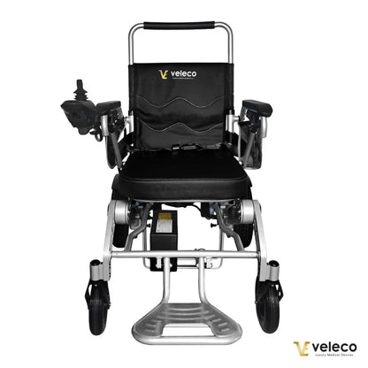 Izdelek na sliki je električni invalidski voziček znamke Veleco, model Cosmo. Voziček ima črno oblazinjenje in robustno aluminijasto konstrukcijo. Na sliki so vidni nadzorni elementi na eni strani, ki omogočajo enostavno upravljanje, ter prostoren sedež, kar zagotavlja udobje uporabniku.