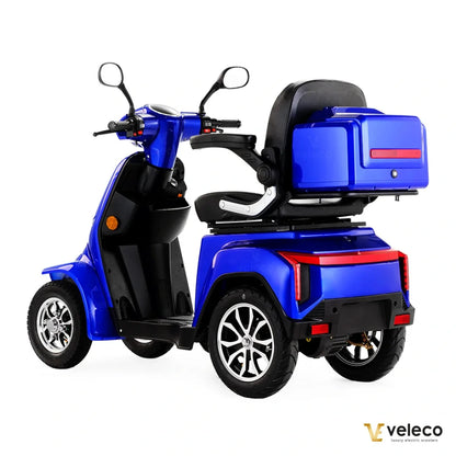 Izdelek je električni skuter, model Veleco Gravis. Na sliki je prikazan modri skuter s tremi kolesi, udobnim sedežem in prostorom za shranjevanje na zadnjem delu. Vidni so tudi krmili in ogledala, kar nakazuje na enostavno upravljanje. Skuter je zasnovan za udobno in varno vožnjo.