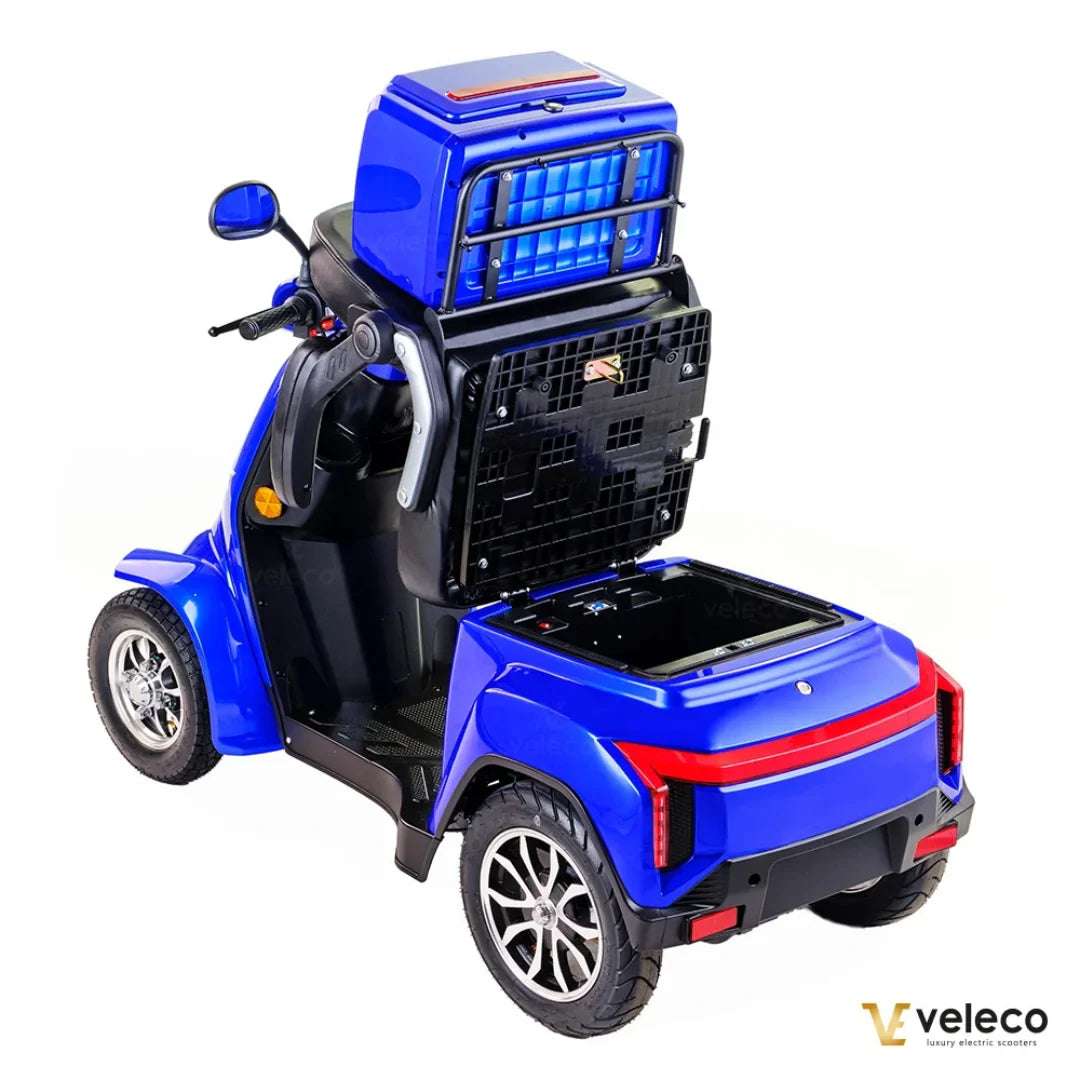 Izdelek na sliki je električni skuter, model Veleco Gravis. Vidna je modra karoserija s prostornim zadnjim predalom za shranjevanje in udobno sedežno površino. Skuter ima tudi široke pnevmatike in moderno oblikovan zadnji del, kar prispeva k njegovi funkcionalnosti in estetiki.