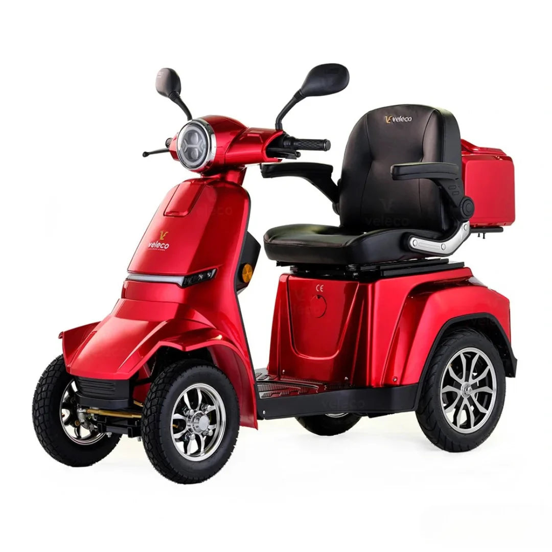 Izdelek na sliki je električni mobilni voziček, model Veleco Gravis. Ima tri kolesa in je zasnovan za udobno prevoznost, kar omogoča enostavno manevriranje. Rdeča barva in ergonomsko oblikovana sedežna enota zagotavljata privlačen videz in udobje med vožnjo. Na zadnjem delu vozička je tudi prostor za shranjevanje.