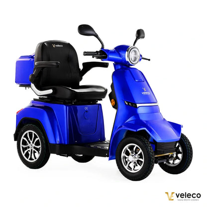 Izdelek na sliki je električni skuter, natančneje model Veleco Gravis. Na sliki je vidna modra barva skuterja, ki ima udobno sedežno mesto z naslonjalom. Skuter je zasnovan za enostavno vožnjo, opremljen je z dvema sprednjima kolesoma in zadnjim prostorom za shranjevanje. Vidna je tudi sprednja luč in krmilo, kar nakazuje na njegovo uporabnost v urbanem okolju.