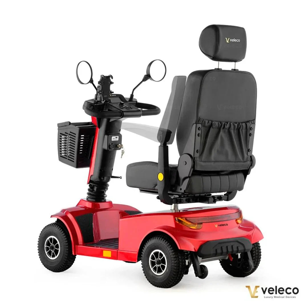 Izdelek na sliki je električni skuter, model Veleco Jumpy. Na sliki je vidna rdeča konstrukcija skuterja, ki ima udoben sedež z naslonjalom, krmilo z ogledali in košarico spredaj. Skuter je zasnovan za udobno vožnjo in enostavno upravljanje, kar ga naredi primernega za različne uporabnike.