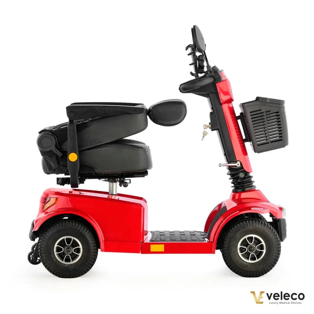 Izdelek je električni skuter, model Veleco Jumpy. Na sliki je prikazan stranski pogled skuterja, ki je v rdeči barvi. Ima udobno črno sedežno površino in prostoren prostor za noge. Na krmilu so vidni ročaji in nadzorna plošča, poleg tega pa je na zadnjem delu skuterja tudi košara za shranjevanje. Skuter je zasnovan za udobno in varno vožnjo.