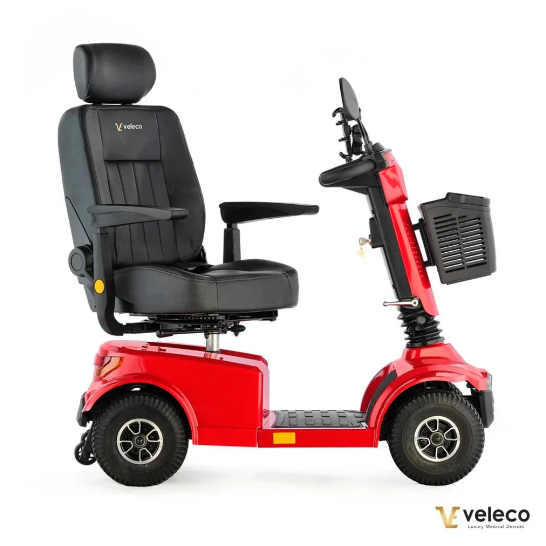 Izdelek na sliki je električni skuter, model Veleco Jumpy. Vidna je udobna sedežna enota s naslonjalom in naslonoma za roke, ter robustna kolesa, kar omogoča enostavno vožnjo. Skuter je v svetlo rdeči barvi in je zasnovan za udobno in varno mobilnost.