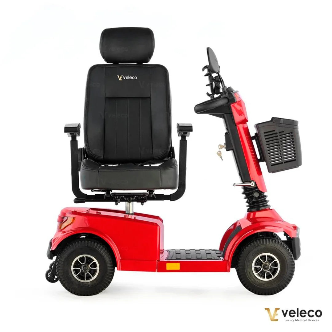 Izdelek je električni skuter, model Veleco Jumpy. Na sliki je prikazan skuter v rdeči barvi, opremljen s širokim udobnim sedežem, ki ima naslon za glavo. Vidni so tudi krmili in prednji del skuterja, ki vključuje prostor za shranjevanje. Skuter je zasnovan za udobno in enostavno mobilnost.