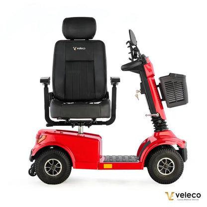 Izdelek je električni skuter, model Veleco Jumpy. Na sliki je prikazan skuter v rdeči barvi, opremljen s širokim udobnim sedežem, ki ima naslon za glavo. Vidni so tudi krmili in prednji del skuterja, ki vključuje prostor za shranjevanje. Skuter je zasnovan za udobno in enostavno mobilnost.