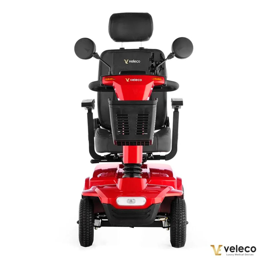 Izdelek je električni skuter, natančneje model Veleco Jumpy. Na sliki je vidna rdeča električna mobilnostna naprava s širokim sedežem in naslonjalom, ki nudi udobje uporabniku. Opremljen je z ročkami za upravljanje, ogledali in prednjim svetlom, kar omogoča enostavno in varno vožnjo. Skuter je zasnovan za udobno premikanje in je primeren za različne uporabnike.