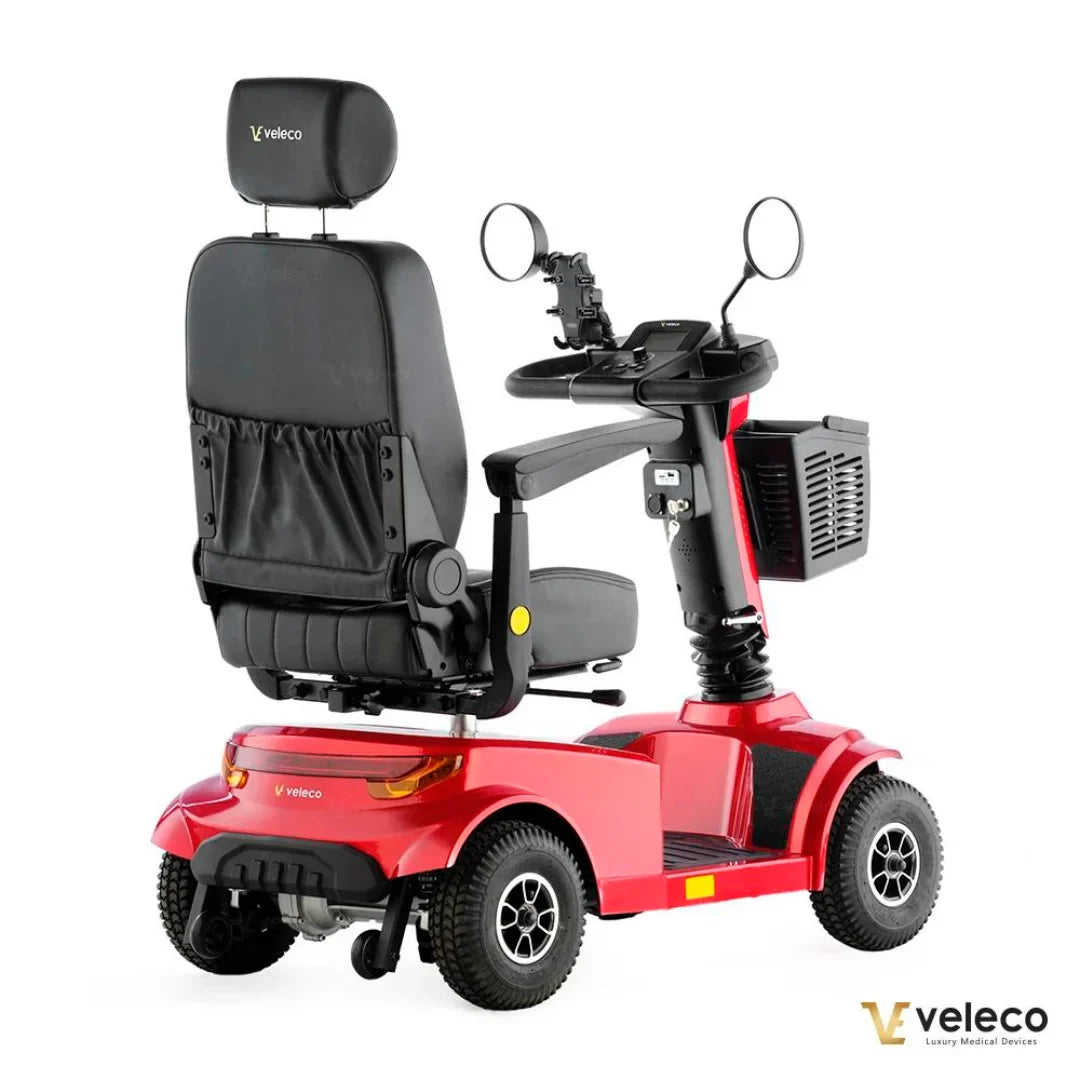 Izdelek na sliki je električni skuter, model Veleco Jumpy. Na sliki je prikazan skuter v rdeči barvi, ki ima udobno sedežno površino s hrbtno oporo, ter krmilo z nadzornimi elementi. Vidni so tudi zadnji in sprednji odbijači ter kolesa, kar nakazuje na njegovo uporabnost za mobilnost. Skuter je zasnovan za udobno in varno vožnjo.