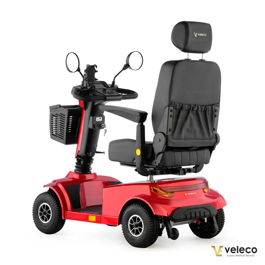 Izdelek je električni skuter, model Veleco Jumpy. Na sliki je vidna rdeča konstrukcija skuterja z udobnim sedežem in krmilom, ki vključuje ogledala. Spredaj je tudi košara za shranjevanje. Skuter je zasnovan za udobno vožnjo in enostavno upravljanje.