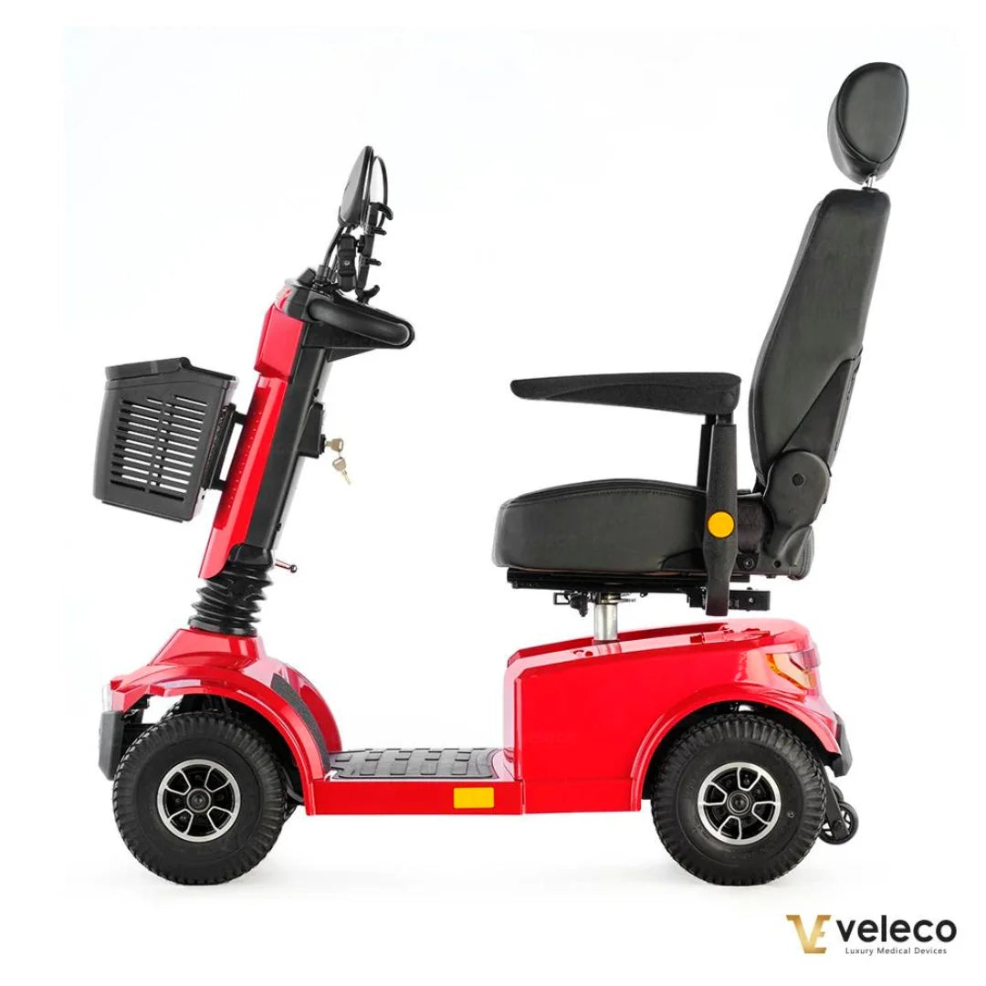 Izdelek na sliki je električni skuter, natančneje model "Jumpy" znamke Veleco. Skuter je v rdeči barvi in ima udobno sedežno površino s naslonjalom ter ročaji za podporo. Na zadnji strani je vidna košarica za shranjevanje, kar povečuje njegovo praktičnost. Kolesa so robustna, kar omogoča stabilno vožnjo.