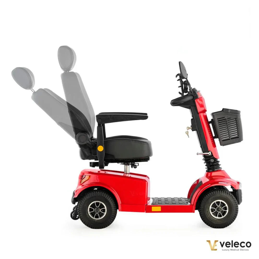 Izdelek na sliki je električni skuter, model Veleco Jumpy. Na sliki je vidna stranska perspektiva skuterja, ki ima udobno sedežno garnituro z nastavljivim naslonom. Skuter je v svetlo rdeči barvi in ima široka kolesa, kar zagotavlja stabilnost in udobno vožnjo. Na zadnjem delu je tudi košara za shranjevanje.