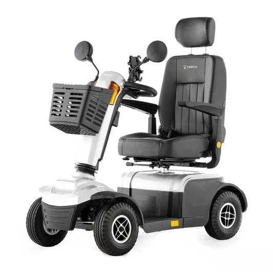 Izdelek na sliki je električni mobilni voziček, model Veleco Looper. Na sliki je prikazan voziček s širokim sedežem in naslonjalom, ki nudi udobje med vožnjo. Ima tudi ročaje za upravljanje in košaro spredaj, kar omogoča enostavno prenašanje manjših predmetov. Kolesa so robustna, kar zagotavlja stabilnost in varnost pri vožnji.