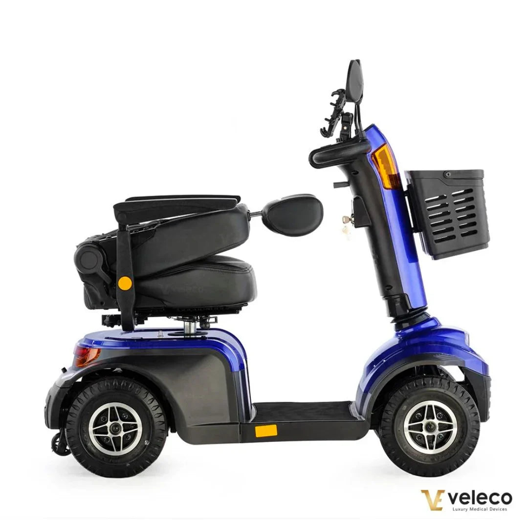 Izdelek na sliki je električni skuter, model Veleco Looper. Skuter ima udoben sedež in je zasnovan za mobilnost, kar omogoča enostavno premikanje. Na sliki so vidni široki kolesi, krmilo z ogledalom ter košara za shranjevanje, kar dodatno povečuje funkcionalnost in udobje pri uporabi.