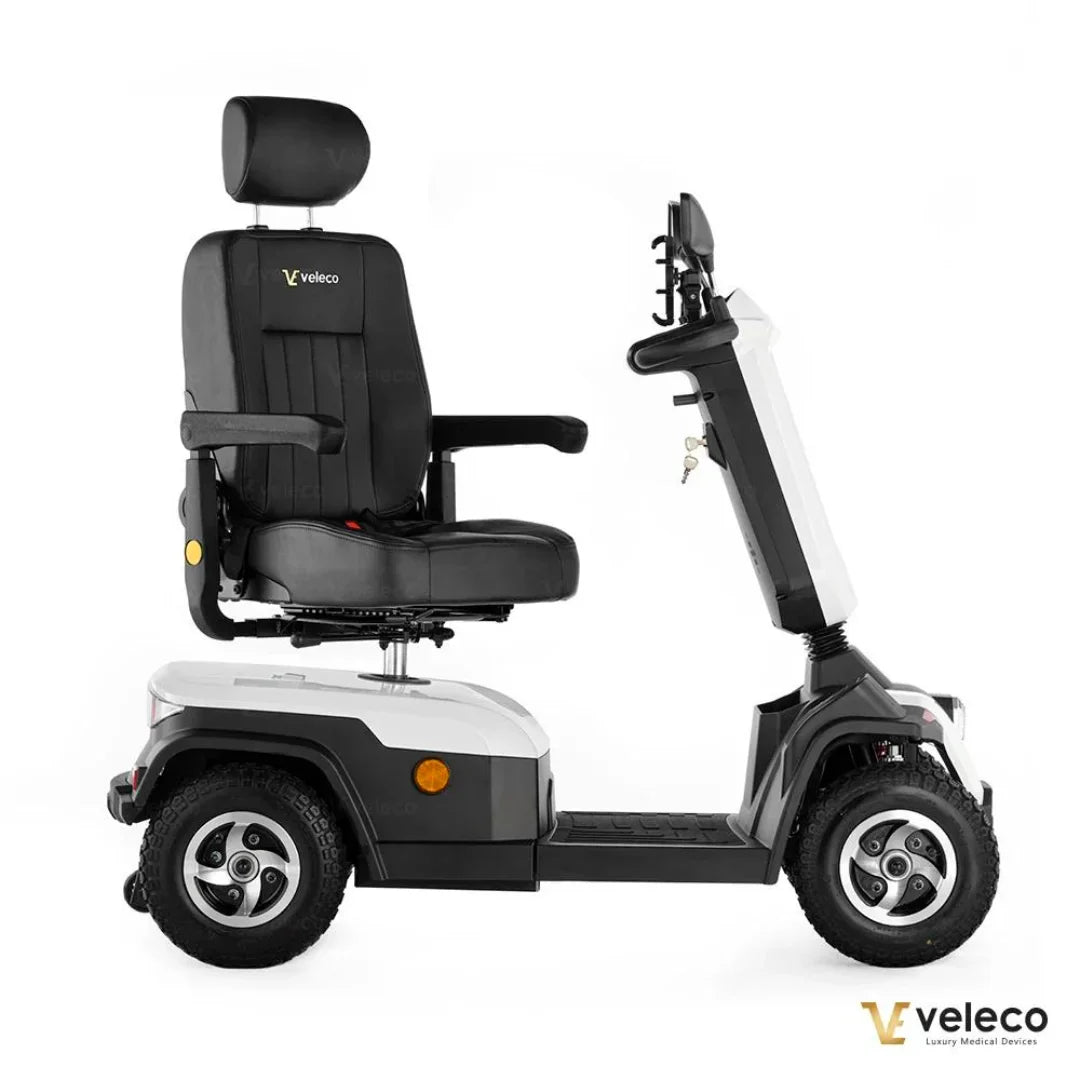 Izdelek je električni skuter, model Veleco Sharpy. Na sliki je prikazan skuter z udobnim sedežem, ki ima naslonjalo in naslone za roke. Skuter je zasnovan za mobilnost, opremljen je z robustnimi kolesi in upravljalno palico na desni strani. Barvna kombinacija vključuje črno in belo, kar daje modern videz.