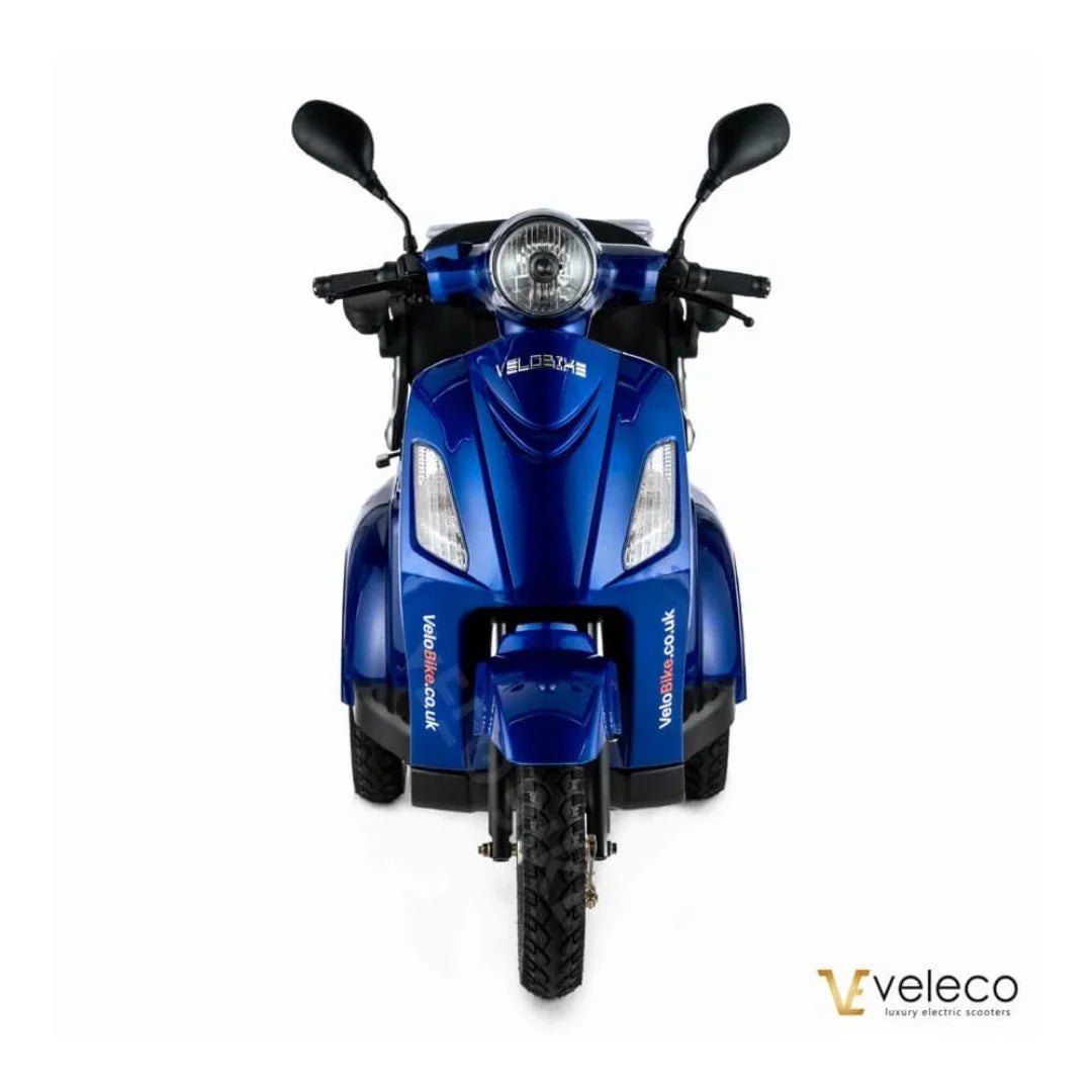 Izdelek na sliki je električni mobilni voziček, model Veleco ZT15. Na sliki je prikazan sprednji del vozička, ki je v svetlo modri barvi. Ima široke pnevmatike, dva krmila in sprednjo luč, kar nakazuje na funkcionalnost in udobje pri vožnji. Znamka Veleco je znana po luksuznih električnih skuterjih.