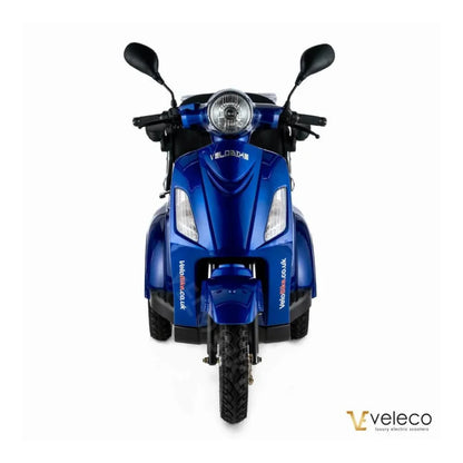 Izdelek na sliki je električni mobilni voziček, model Veleco ZT15. Na sliki je prikazan sprednji del vozička, ki je v svetlo modri barvi. Ima široke pnevmatike, dva krmila in sprednjo luč, kar nakazuje na funkcionalnost in udobje pri vožnji. Znamka Veleco je znana po luksuznih električnih skuterjih.