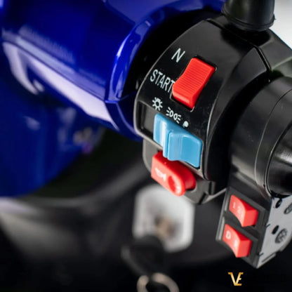 Izdelek je električni mobilni voziček, model Veleco ZT15. Na sliki so prikazani nadzorni gumbi in stikala vozička, ki vključujejo gumb za zagon, nastavitve hitrosti in druge funkcionalnosti. Barva vozička je modra, kar daje sodoben videz.