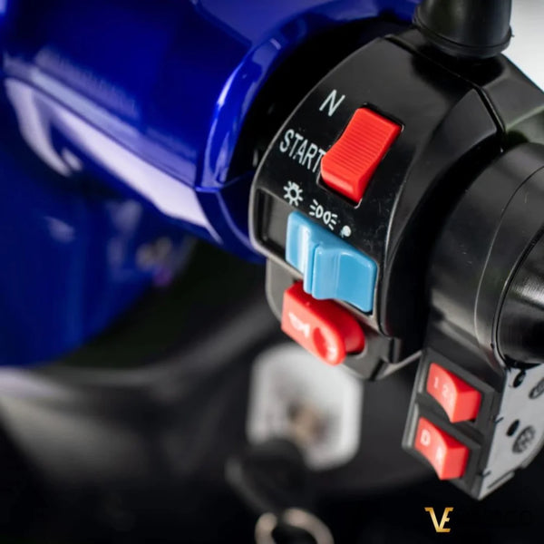 Izdelek je električni mobilni voziček, model Veleco ZT15. Na sliki so prikazani nadzorni gumbi in stikala vozička, ki vključujejo gumb za zagon, nastavitve hitrosti in druge funkcionalnosti. Barva vozička je modra, kar daje sodoben videz.