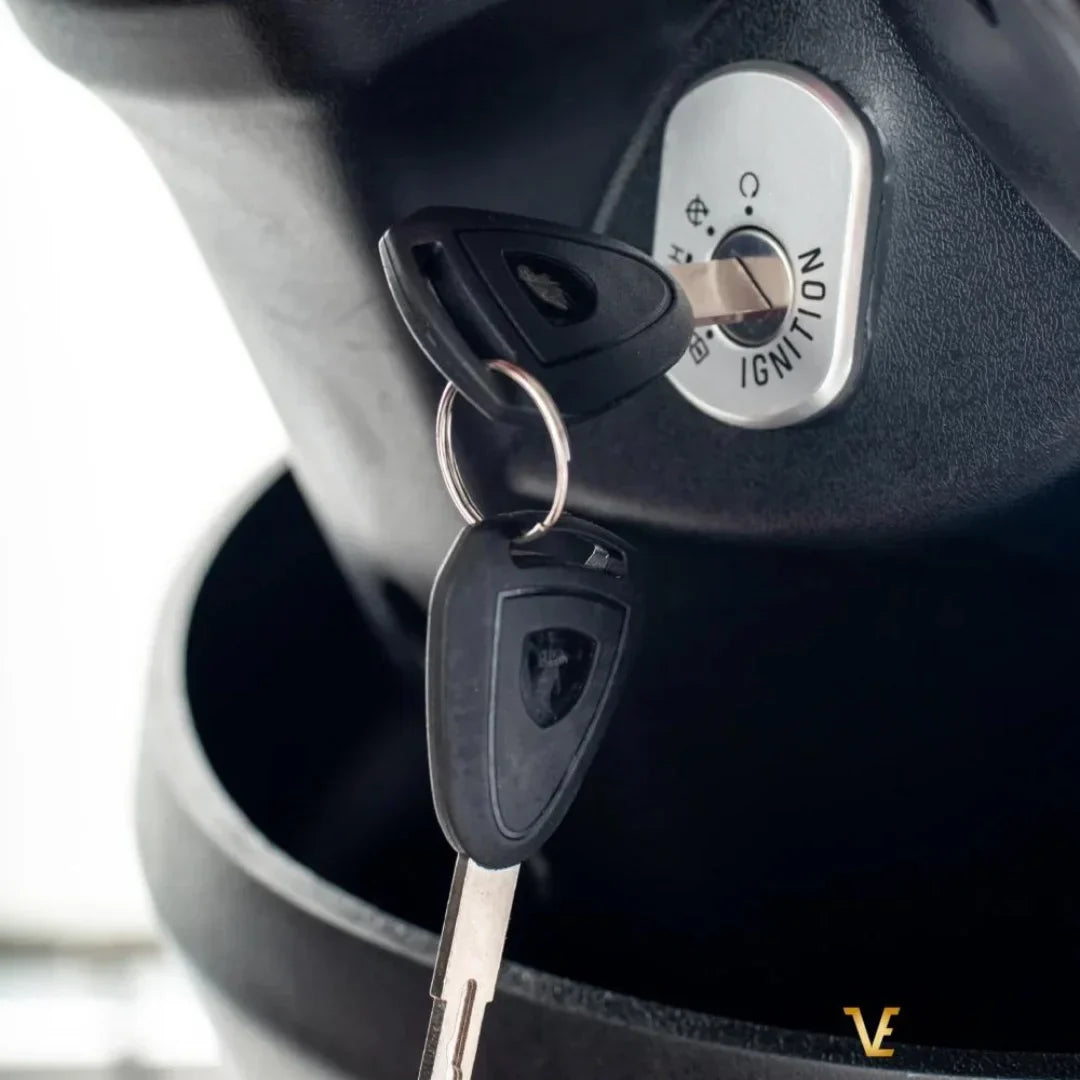 Izdelek je električni mobilni voziček, model Veleco ZT15. Na sliki je prikazan ključ za vžig, ki je vključen v ključavnico vozička. Vidna je tudi oznaka "IGNITION", kar nakazuje na funkcionalnost vžiga. Voziček je zasnovan za enostavno upravljanje in mobilnost.