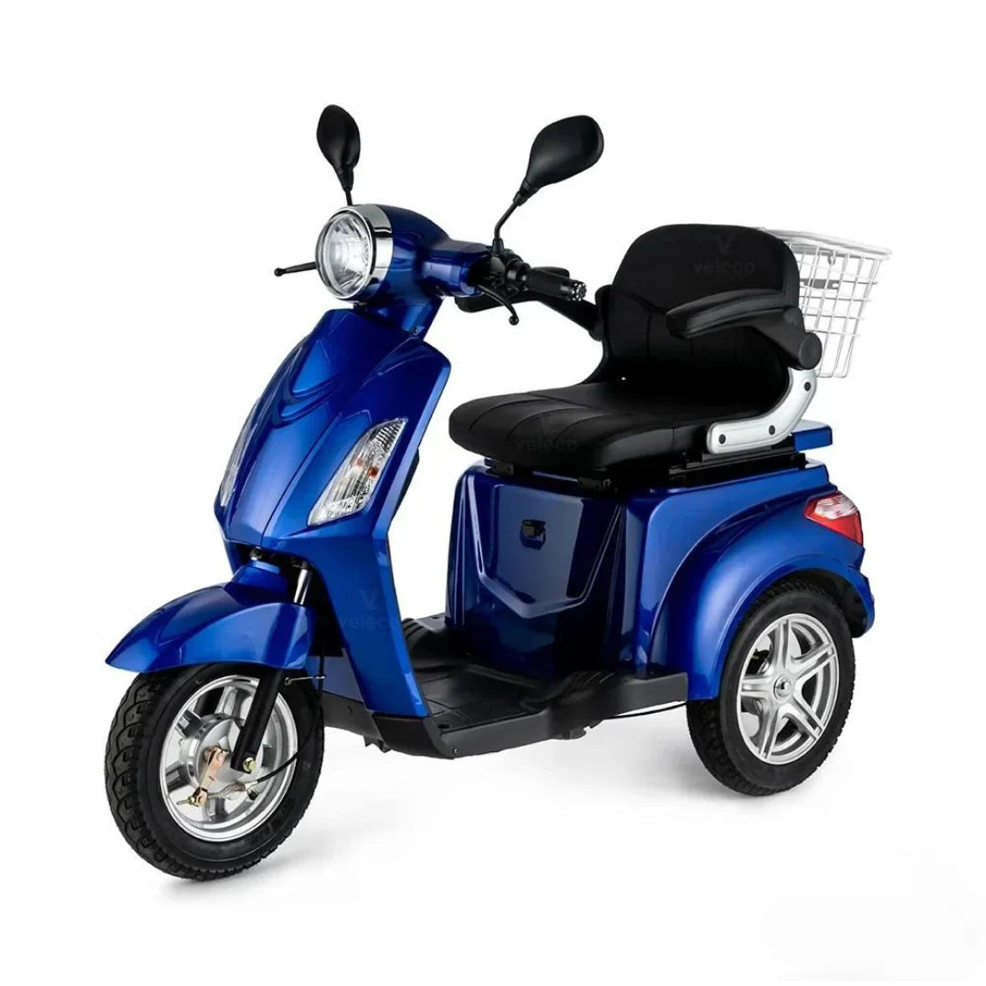 Izdelek je električni mobilni voziček, model Veleco ZT15. Na sliki je prikazan voziček v modri barvi, ki ima udobno sedežno površino in sprednji del, podoben skuterju. Na zadnjem delu je košara za shranjevanje, kar omogoča praktično uporabo. Vozilo je zasnovano za enostavno manevriranje in udobno vožnjo.