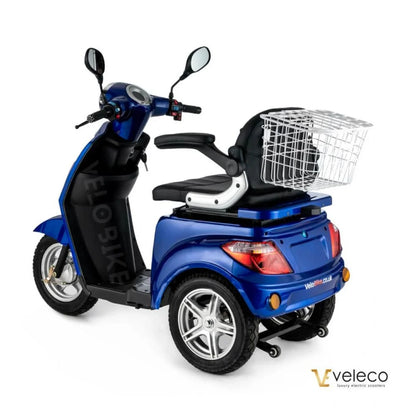 Izdelek je električni mobilni voziček, model Veleco ZT15. Na sliki je prikazan voziček v modri barvi, opremljen z udobnim sedežem in prednjim košem za shranjevanje. Ima dva velika kolesa in krmilo z ogledali, kar omogoča enostavno manevriranje.