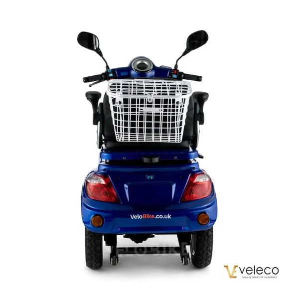 Izdelek na sliki je električni mobilni voziček, model Veleco ZT15. Na sliki je vidna zadnja stran vozička, ki ima široka kolesa in udobno sedežno mesto. Na vrhu je nameščen koš za shranjevanje, kar omogoča enostavno prevažanje manjših predmetov. Voziček je v modri barvi in ima elegantno obliko, kar ga naredi privlačnega za uporabnike.