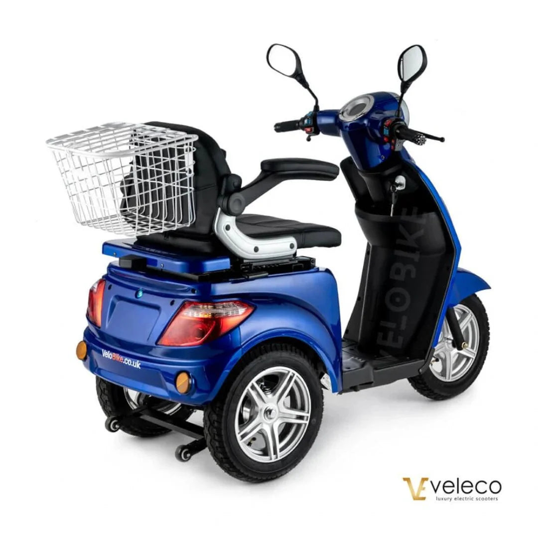 Izdelek je električni mobilni voziček, model Veleco ZT15. Na sliki je vidna modra električna vozila s tremi kolesi, ki ima udobno sedežno mesto in ročaj za upravljanje. Na zadnjem delu vozička je nameščen kovinski koš za shranjevanje, kar povečuje njegovo funkcionalnost. Vozilo je zasnovano za enostavno uporabo in mobilnost.