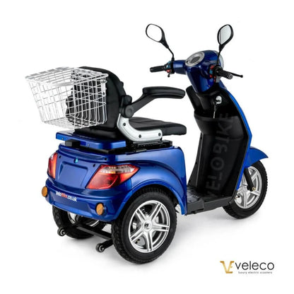 Izdelek je električni mobilni voziček, model Veleco ZT15. Na sliki je vidna modra električna vozila s tremi kolesi, ki ima udobno sedežno mesto in ročaj za upravljanje. Na zadnjem delu vozička je nameščen kovinski koš za shranjevanje, kar povečuje njegovo funkcionalnost. Vozilo je zasnovano za enostavno uporabo in mobilnost.