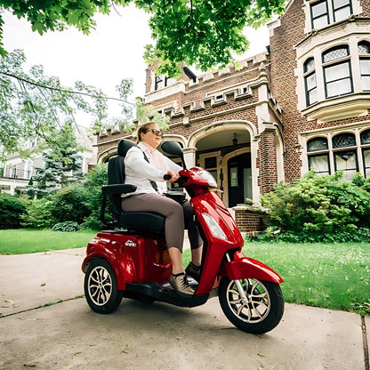 Ženska se vozi z električnim mobilnim vozičkom Veleco Zt15 pred veliko hišo iz opeke.