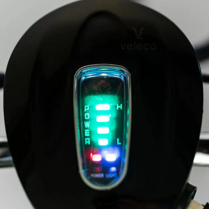 Izdelek je električni mobilni voziček, model Veleco ZT16. Na sliki je prikazan del nadzorne plošče, kjer so vidni LED indikatorji za moč in nivo baterije. Indikatorji so osvetljeni v različnih barvah, kar uporabniku omogoča enostavno spremljanje stanja vozička. Znamka Veleco je znana po svojih električnih mobilnih rešitvah.