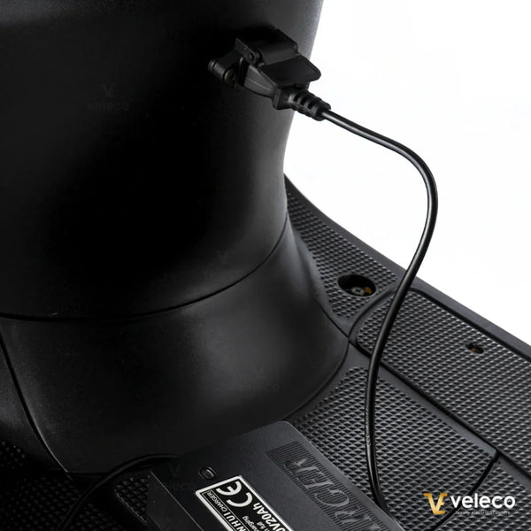 Izdelek je električni mobilni voziček, model Veleco ZT63. Na sliki je prikazan del vozička, kjer je vidna povezava za polnjenje, ki je povezana z električnim sistemom. Površina vozička je narejena iz materiala, ki nudi dober oprijem, kar je pomembno za varno uporabo.