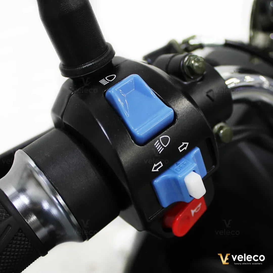 Izdelek je električni mobilni voziček, model Veleco ZT63. Na sliki je prikazan del krmiljenja, kjer so vidni različni gumbi, vključno z gumbom za luči in smerokaze. Gumbi so v modri in rdeči barvi, kar omogoča enostavno upravljanje vozila.