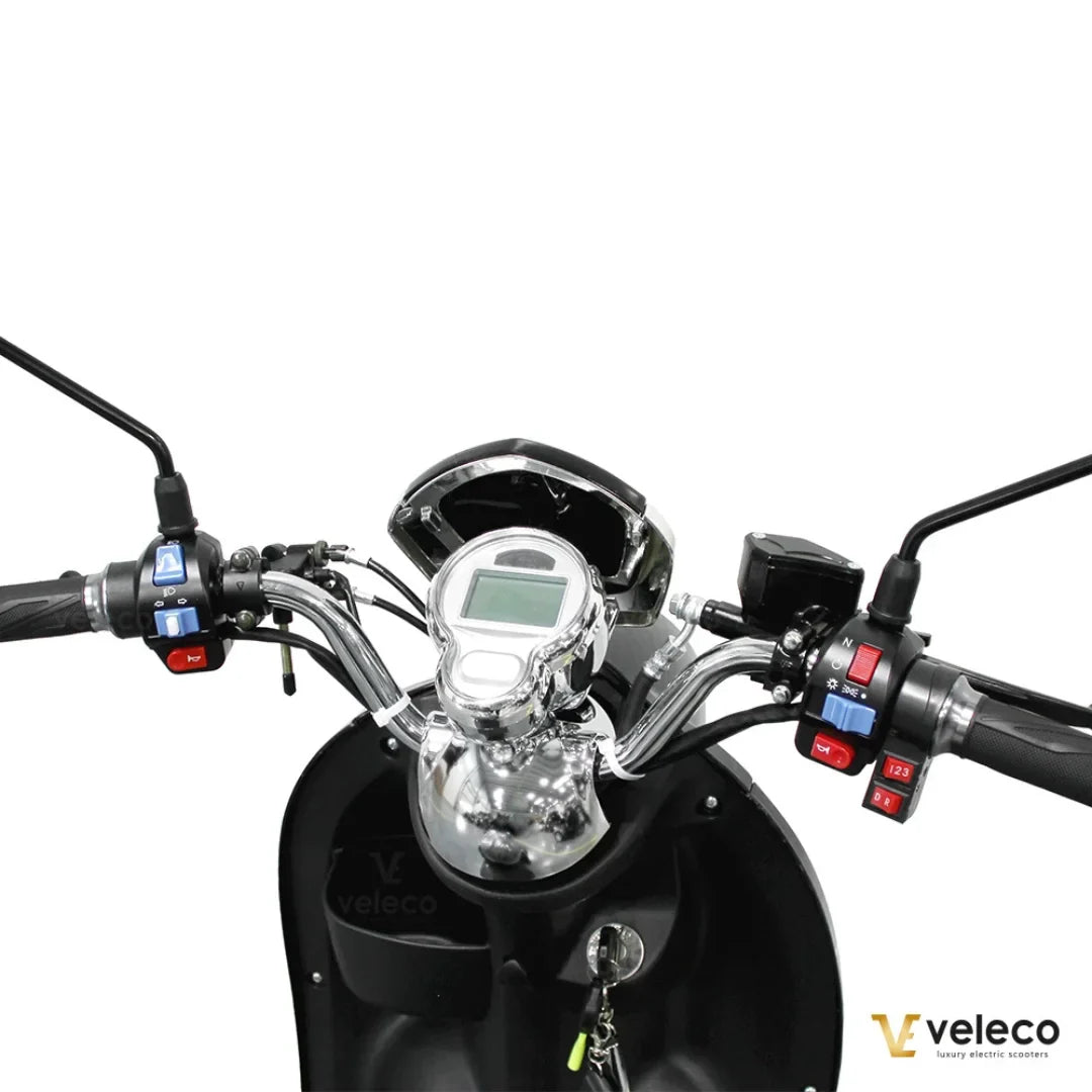 Izdelek je električni mobilni voziček, model Veleco ZT63. Na sliki je prikazan krmni del vozička, kjer so vidni ročaji, merilnik hitrosti in različni gumbi za upravljanje. Krmilo je oblikovano za enostavno uporabo, kar omogoča udobno vožnjo. Zasnova vključuje tudi ključavnico, kar povečuje varnost.