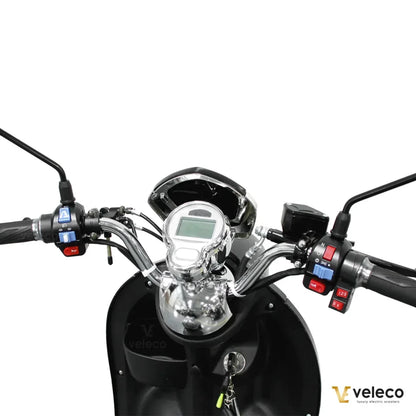 Izdelek je električni mobilni voziček, model Veleco ZT63. Na sliki je prikazan krmni del vozička, kjer so vidni ročaji, merilnik hitrosti in različni gumbi za upravljanje. Krmilo je oblikovano za enostavno uporabo, kar omogoča udobno vožnjo. Zasnova vključuje tudi ključavnico, kar povečuje varnost.