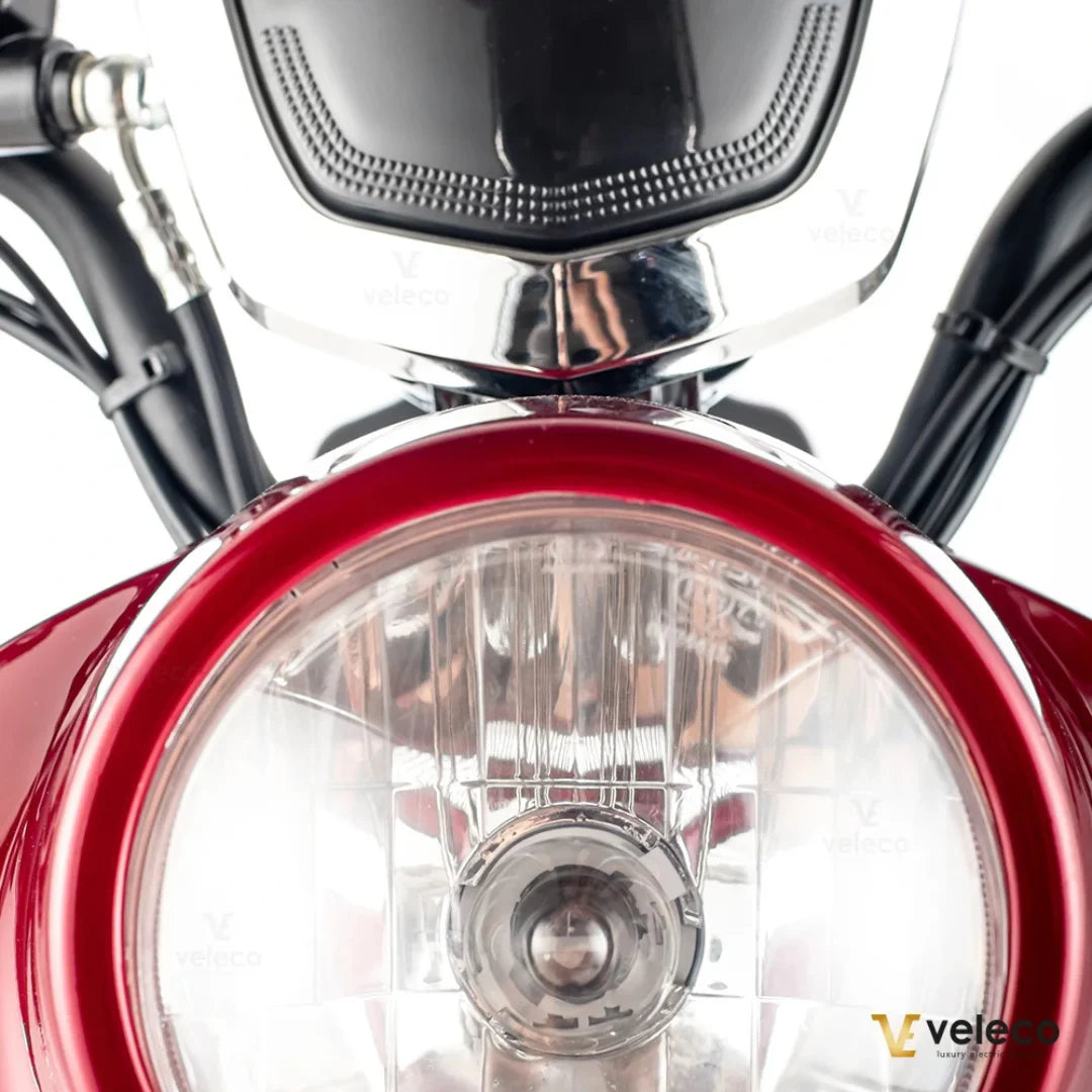 Izdelek je električni mobilni voziček, model ZT63, znamke Veleco. Na sliki je prikazan sprednji del vozička, kjer je vidna svetilka v rdeči obrobi ter kromirani detajli, ki dodajajo eleganten videz. Voziček ima robustno zasnovo, kar nakazuje na udobno in varno vožnjo.