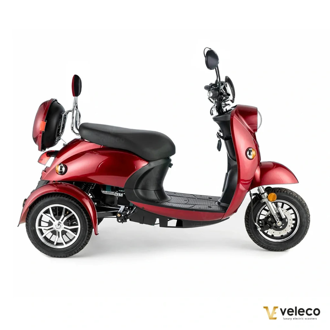 Izdelek je električni mobilni voziček, model Veleco ZT63. Na sliki je prikazan voziček v rdeči barvi s širokim sedežem in prostornim stopalom. Ima tri kolesa, kar zagotavlja stabilnost, ter je opremljen z ogledali in prednjim svetilom. Zasnova je moderna in primerna za udobno vožnjo.