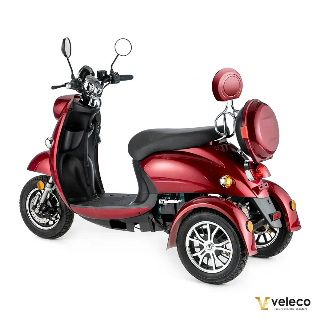 Izdelek je električni mobilni voziček, model Veleco ZT63. Na sliki je videti eleganten voziček v rdeči barvi, opremljen s tremi kolesi za stabilnost. Ima udobno sedežno površino in je zasnovan za enostavno vožnjo, kar ga naredi primernega za različne uporabnike. Na krmilu so nameščeni ogledali, kar povečuje varnost med vožnjo.