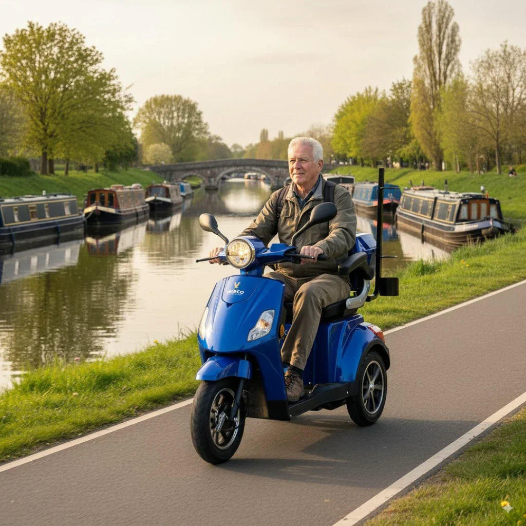Na sliki je električni skuter, model Veleco Draco. Izdelek je v svetlo modri barvi in se uporablja za prevoz po kolesarskih poteh. Na skuterju sedi starejši moški, ki uživa v vožnji ob reki, obkrožen z naravo in plovili na vodi.