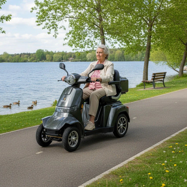 Izdelek je električni skuter, znamke Veleco, model Gravis. Na sliki vidimo starejšo osebo, ki vozi skuter ob jezeru, obdanem z zelenjem in drevesi. Skuter ima tri kolesa, kar zagotavlja stabilnost, in je zasnovan za udobno vožnjo. V ozadju so vidne tudi klopi in ptice, kar ustvarja prijetno naravno okolje.